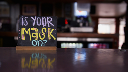 a hand-written chalk sign sitting on a counter in a restaurant reads: is your mask on?