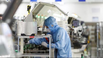 An employee clad in head-to-toe protective equipment works in a semiconductor factory.