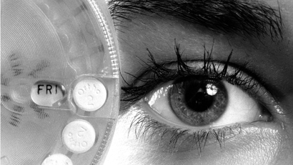 A birth control wheel held up to a face with mascara on the eye lid.