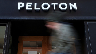A person walks past a Peloton store with the company's name pictured in white letters above.