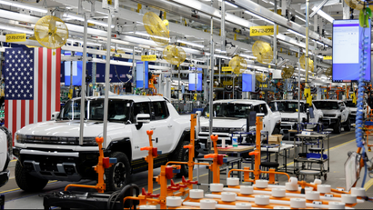 A row of hulking Hummer EV pickup trucks sits on a factory production line.