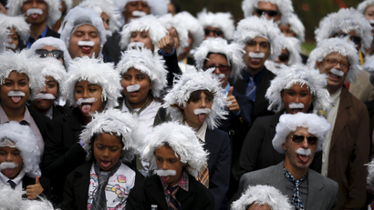 Kids and adults in Einstein-like wigs and mustaches, wearing suits.