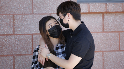 A man hugging a woman, both with masks on.