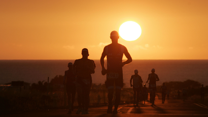 Runners cresting a hill with the sun in the background.