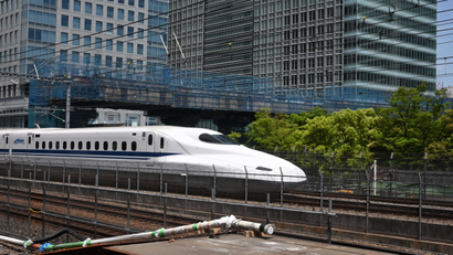 A high-speed train moves on tracks in front of office tower buildings