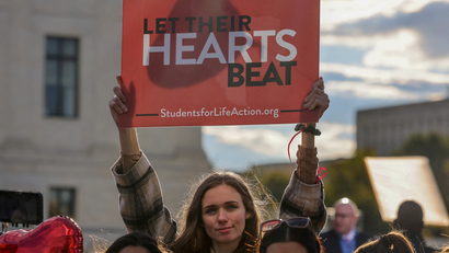 An anti-choice protester holds a sign that reads "let their hearts beat"