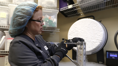 A person in a hairnet, sweatshirt, and gloves opens up a freezer of liquid nitrogen where human eggs are stored.