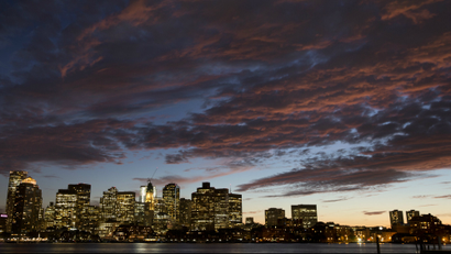 The sunset illuminates clouds over Boston harbor and the city skyline