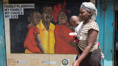 A woman carrying a baby walks past a mural showing a man, woman and child.