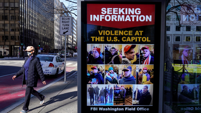 A pedestrian walks past a sign at the bus stop from the FBI seeking information on supporters of U.S. President Donald Trump who stormed the U.S. Capitol