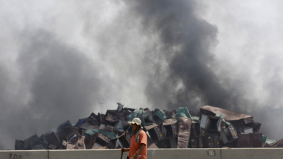 A worker walks as smokes rises near the site of the explosions at the Binhai new district, Tianjin