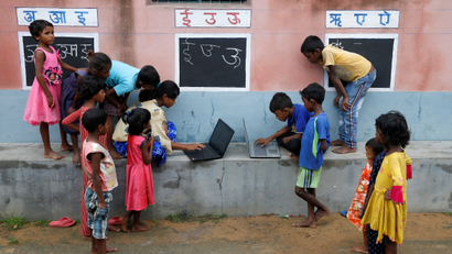 Children use laptops in an open-air class outside a house with the walls converted into black boards at Joba Attpara village