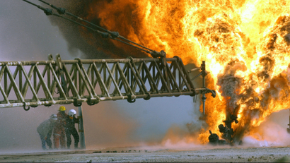 Kuwaiti firefighters secure a burning oil well in the Rumaila oilfields, March 27, 2003, set ablaze by Iraqi military forces. Efforts are underway to extinguish fires and protect the region from environmental disaster.
