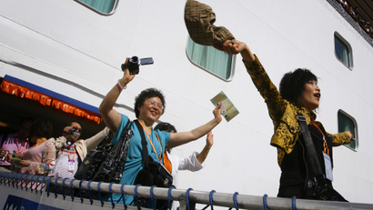 Tourists from China wave as they arrive on a cruise ship in the northern Taiwan port of Keelung March 16, 2009. A total of 1,600 employees from Amway China arrived on Monday, the first large-scale tour group from the mainland via a foreign-owned cruise ship since the opening of direct transport links from the mainland last year. REUTERS/Nicky Loh (TAIWAN POLITICS TRAVEL BUSINESS IMAGE OF THE DAY TOP PICTURE) - RTXCU5A