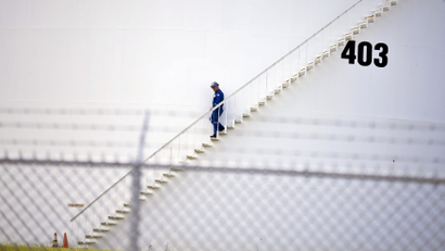 A refinery worker walks down the outside of a storage tank.