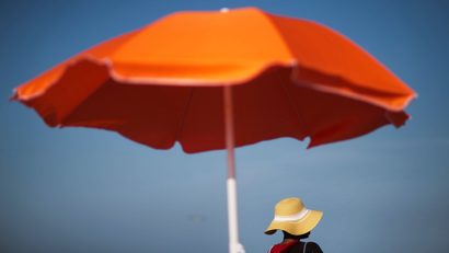 Someone in a brimmed hat sitting under a big orange umbrella