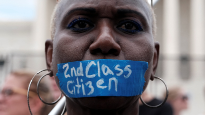 A Black woman wears tape on her mouth reading "2nd class citizen"