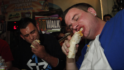 Two diners take big bites of giant burritos.