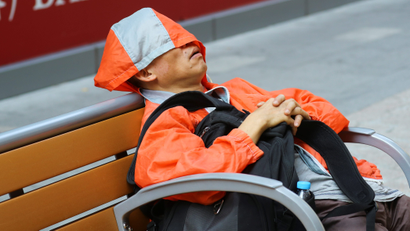 Man in orange jacket asleep on a bench.