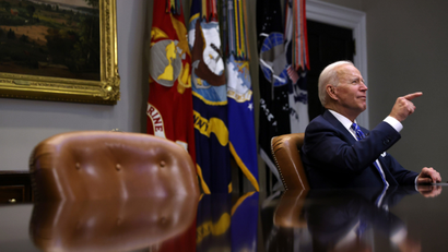US president Joe Biden sits at a conference table and points.