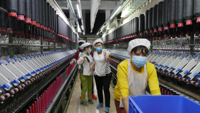 A masked woman rolls away carts of unused tools between rows of spinning machine at a factory owned by Hong Kong's Novetex Textiles Limited in Zhuhai City, Guangdong Province