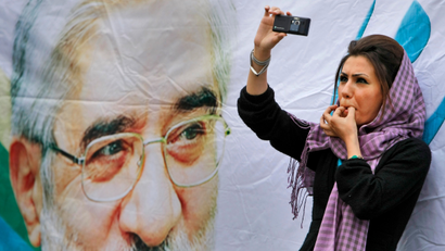 In this June 9, 2009 file picture, a supporter of main challenger and reformist candidate Mir Hossein Mousavi, standing next to a poster of him, whistles as she films the event with her mobile phone, amidst a festive atmosphere at an election rally at the Heidarnia stadium in Tehran, Iran. An opposition activist spreads word of an upcoming protest in the streets of Tehran. Another posts pictures of clashes between demonstrators and police. As Iran's government cracks down on traditional media after the country's disputed presidential election, tech-savvy Iranians have turned to the microblogging site Twitter.