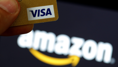 A visa credit card is held in front of an Amazon logo in this picture illustration