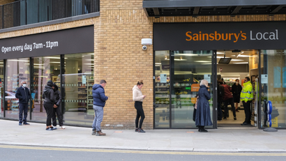 People wait in line to shop at a Sainbury's Local in London.