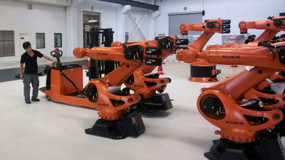A staff member stands next to robots at a plant of Kuka Robotics in Shanghai
