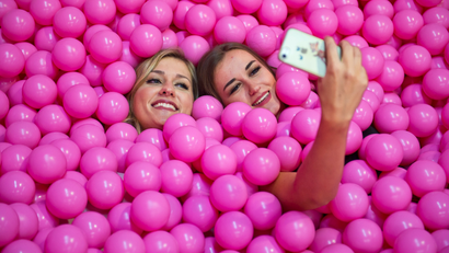 Women lying surrounded by pink plastic balls taking a selfie
