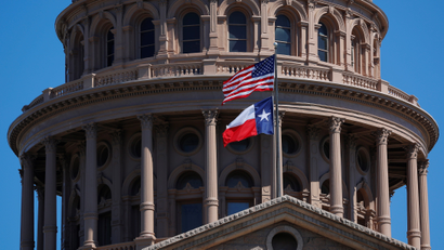The American flag and Texas state flag fly outside the dome of the Texas state capitol building