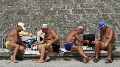 Elderly men play chess on a public beach near the Dnipro river.