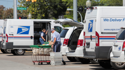 United States Postal Service (USPS) workers load mail into delivery trucks outside a post office.