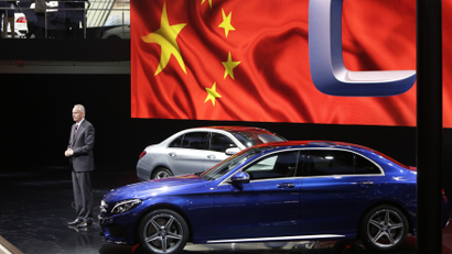 A Daimler board member presents a new car in front of a projection of a Chinese flag.