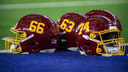 Three Washington Football Team helmets are pictured on a stadium field.
