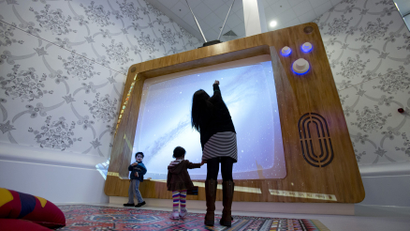 A woman and young children interact with a giant television set