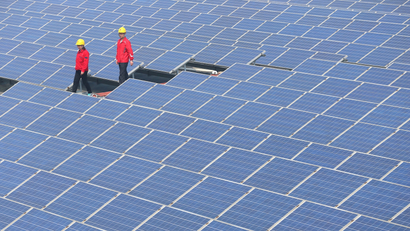 Workers walk past solar panels in Jimo
