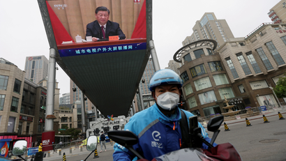 A delivery worker in Beijing near a giant TV screen showing Chinese leader Xi Jinping.