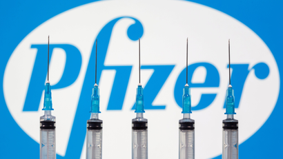 Syringes are seen in front of a Pfizer logo