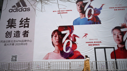 A woman wearing a face mask walks past a banner advertising new Adidas store in Beijing