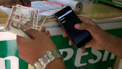 A customer conducts a mobile money transfer, known as M-Pesa, at a Safaricom agent stall, as he holds Kenyan shillings (KSh) in Nairobi, Kenya October 16, 2018.
