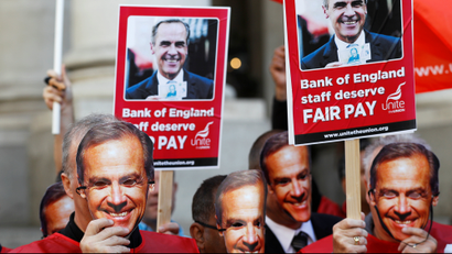 Protesters hold up Bank of England Governor Mark Carney masks outside the bank as it staff begins a three day strike over pay