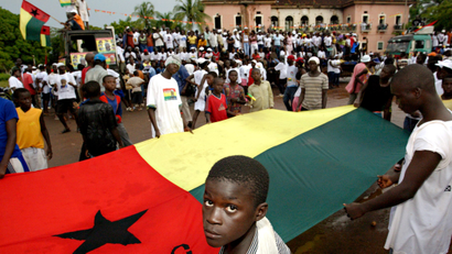 A child looks into a camera as he and other people hold a flag of Guinea Bissau during a political rally