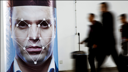 People walk past a poster simulating facial recognition software