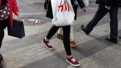 Women with Zara (L) and H&M (C) shopping bags walk at a shopping district