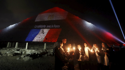 Egyptians light candles as the French and Egyptian flags and France's national colors of blue, white and red are projected onto one of the Giza pyramids, in tribute to the victims of the Paris attacks, on the outskirts of Cairo, Egypt, November 15, 2015.