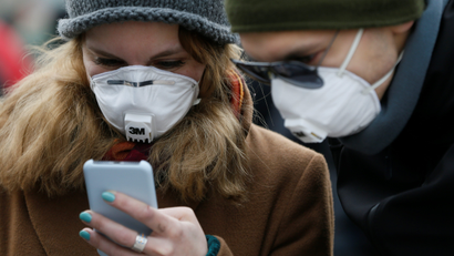 People wearing protective face masks use a smartphone