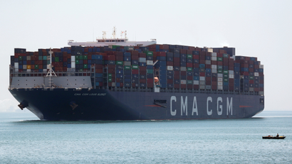 A fisherman travels on a boat in front of a CMA CGM container ship passing through the Suez Canal.