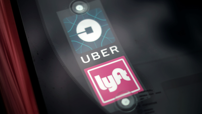 a sign in a car windshield displays a blue logo for Uber and a pink logo for Lyft