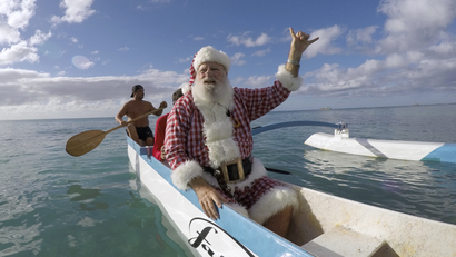 Donald Boyce, dressed up like Santa Claus, waves to surfers as he goes outrigger canoe surfing off Waikiki beach in Honolulu, Hawaii December 13, 2014.